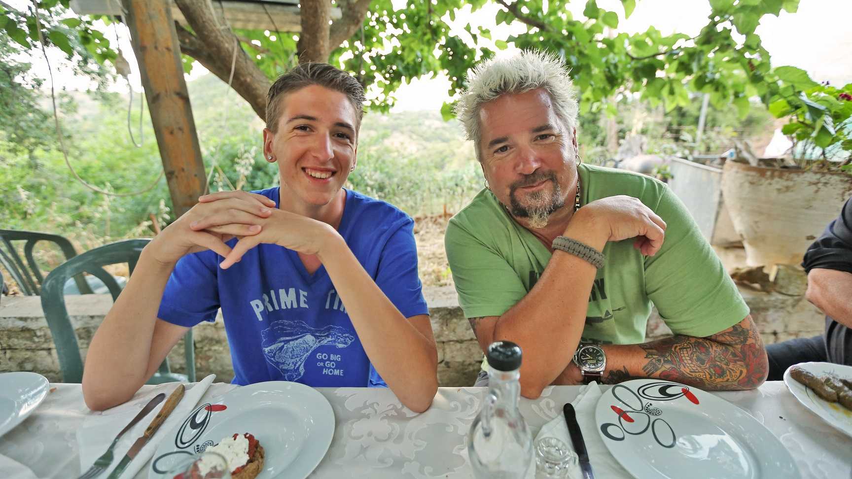 Portrait shot of Guy and Hunter Fieri in Crete,Greece, where they are sitting down for a traditional Greek dinner outside on a terrace, as seen on Food Network's Guy's European Vacation, The Epic Culinary Adventure Special.