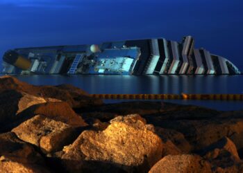 2E0GBXW The wreckage of capsized cruise liner Costa Concordia is seen at night at Giglio Island, Italy on June 20, 2012. Salvage crews began preliminary work on preparations to refloat the half-submerged Costa Concordia cruise liner in what is set to be the biggest ever operation of its kind. A barge has moved next to the liner and the ship's radar has been removed from the upper deck. The swimming pool slide and the large yellow funnel will be taken off in coming weeks.The 290-metre-long (951 feet) cruise liner, operated by Carnival Corp's Costa Cruises unit, capsized off the Tuscan island of Giglio